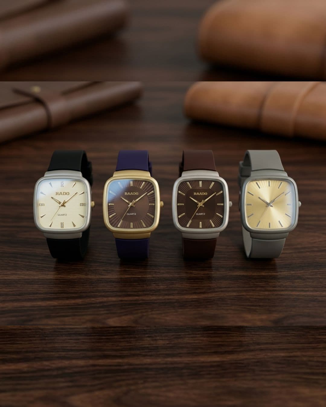 Four RAINO square analog wristwatches with square dials and different straps (black, navy blue, brown, and gray) lined up on a dark wooden table with blurred leather accessories in the background.
