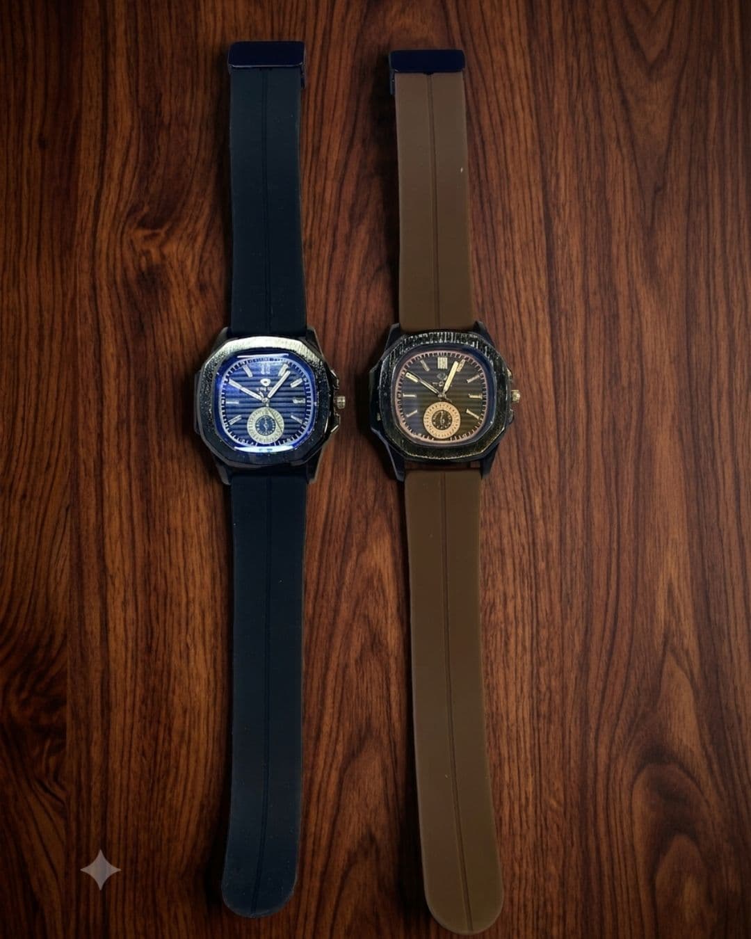 Two rugged smartwatches with square bezels displayed side-by-side on a dark wood background. The watch on the left has a dark blue dial and a dark navy strap.